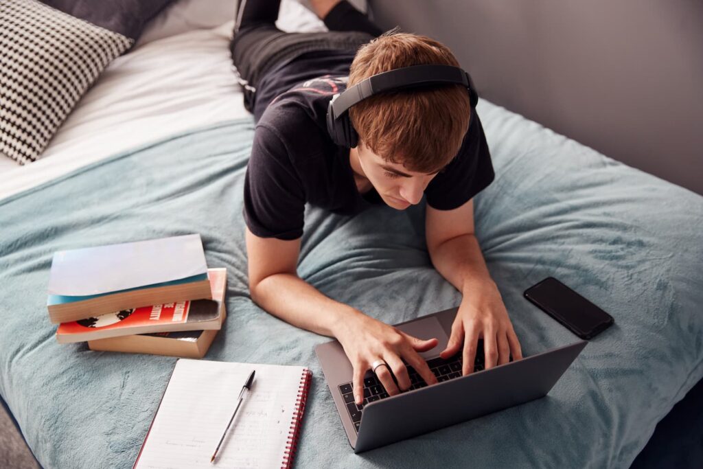 looking-down-on-male-college-student-wearing-headphones-lying-on-bed-working-on-laptop (1)