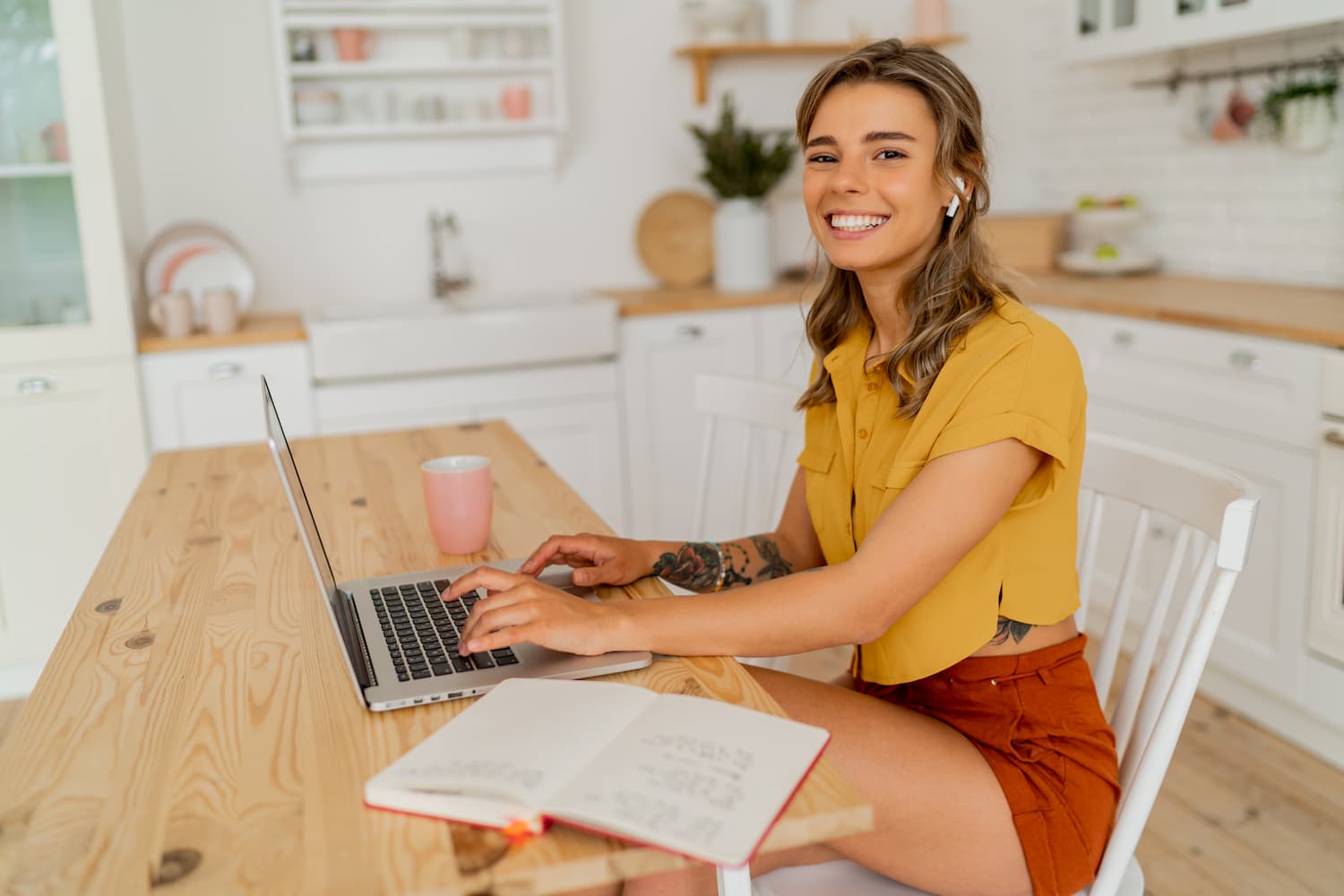 pretty-miling-student-woman-using-laptop-and-writing-notes-on-her-modern-light-kitchen (1)