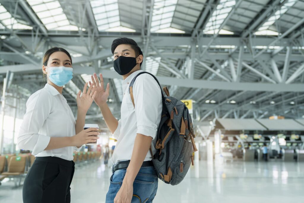 two-attractive-asian-businessman-and-businesswoman-wear-face-mask-protection-hand-gesture-wave-greeting-and-goodbye-social-distancing-in-departure-airport-terminal (1)